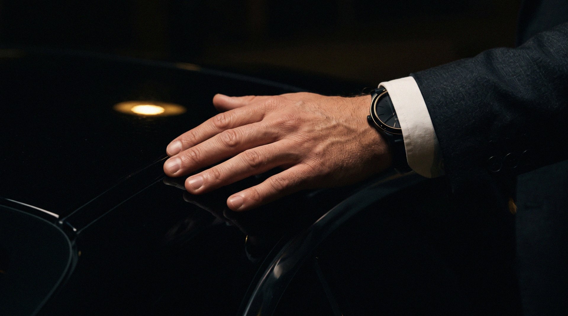 A hand resting on a dark car bonnet, watch detail